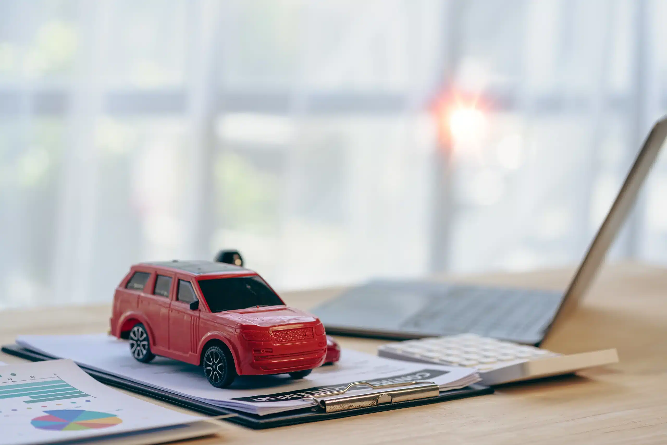 Small red toy car on financial charts next to a laptop, representing car accident claim costs