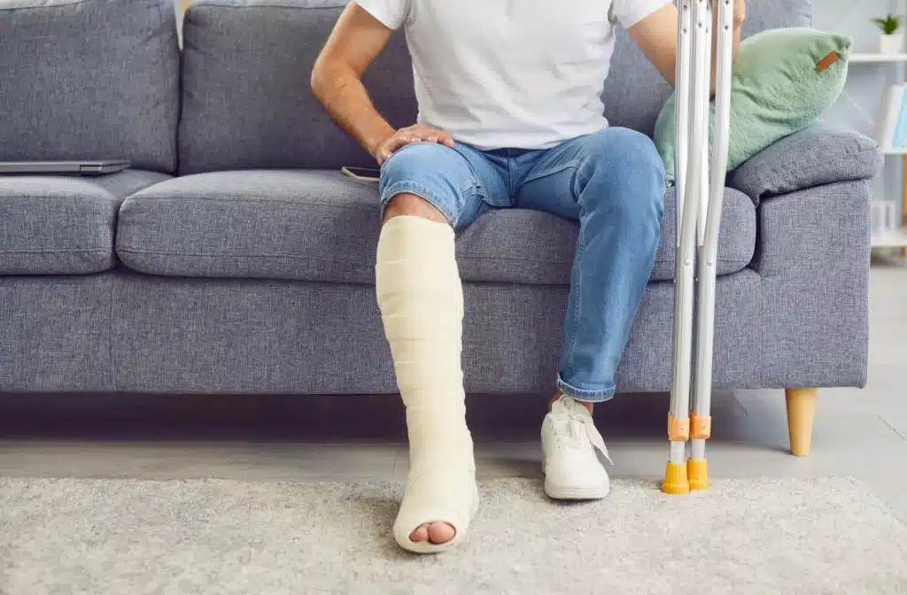 Person sitting on a couch with a leg cast, illustrating a serious injury that could be worsened in a car accident.
