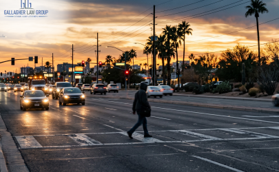 Pedestrian crossing a wide, busy Phoenix intersection at dusk near an unmarked crosswalk