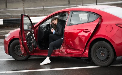 Driver stepping out of a red sedan with side-impact damage after a car accident.